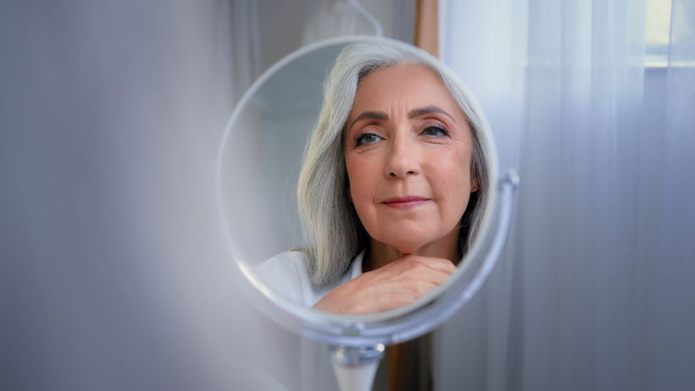 Mirror reflection female wrinkled face 50s middle-aged Caucasian woman senior lady looking self